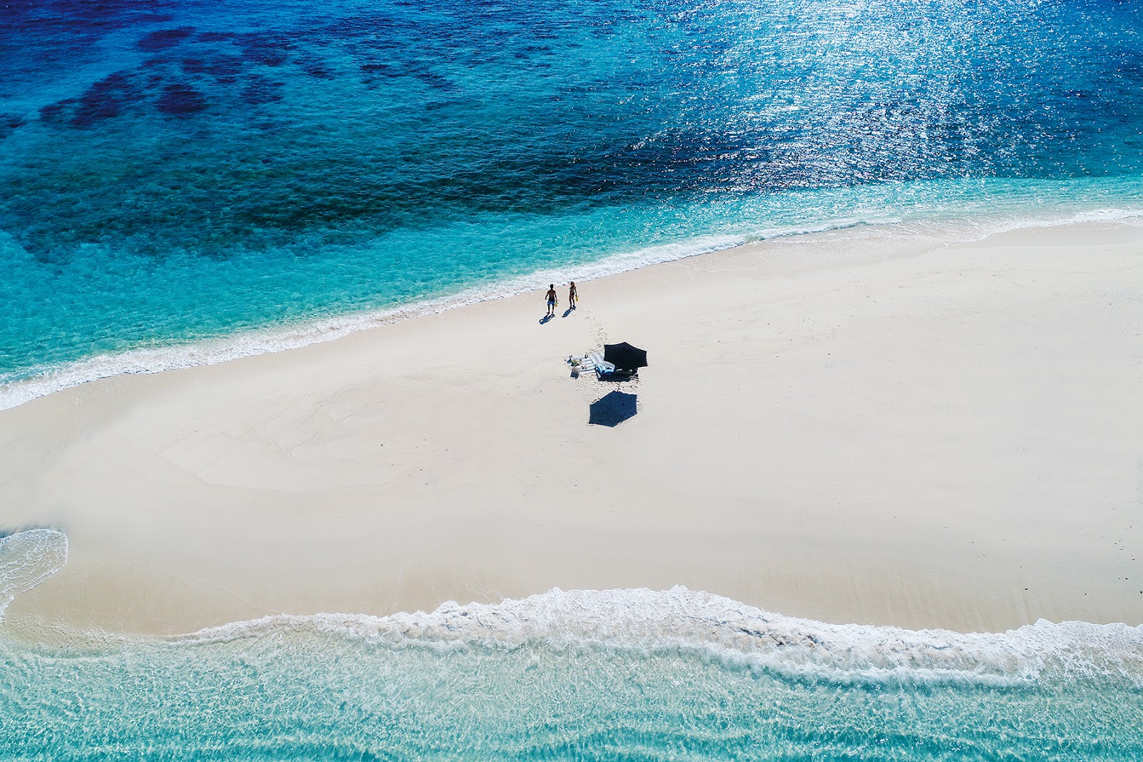 Two guests walk on white sand beside turquoise water with beach umbrellas at Yasawa Island Resort & Spa.