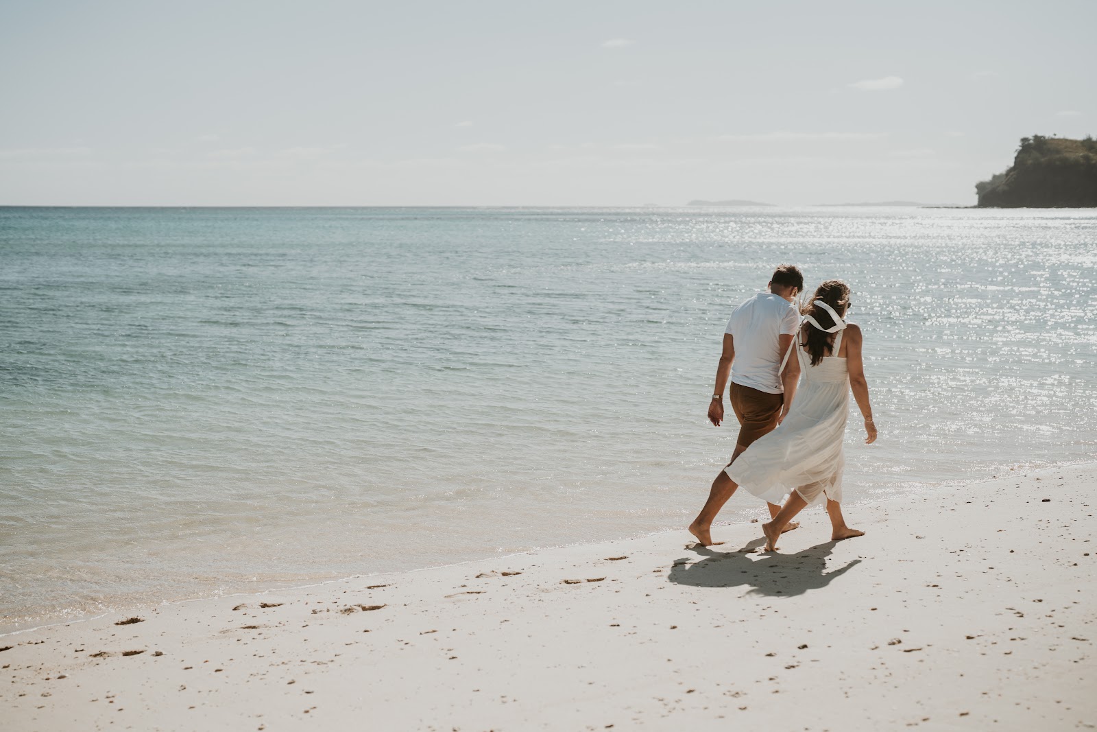 White sand beach with turquoise water and palm fronds overhead, forested hillside visible along the curved shoreline at Yasawa Island Resort & Spa.