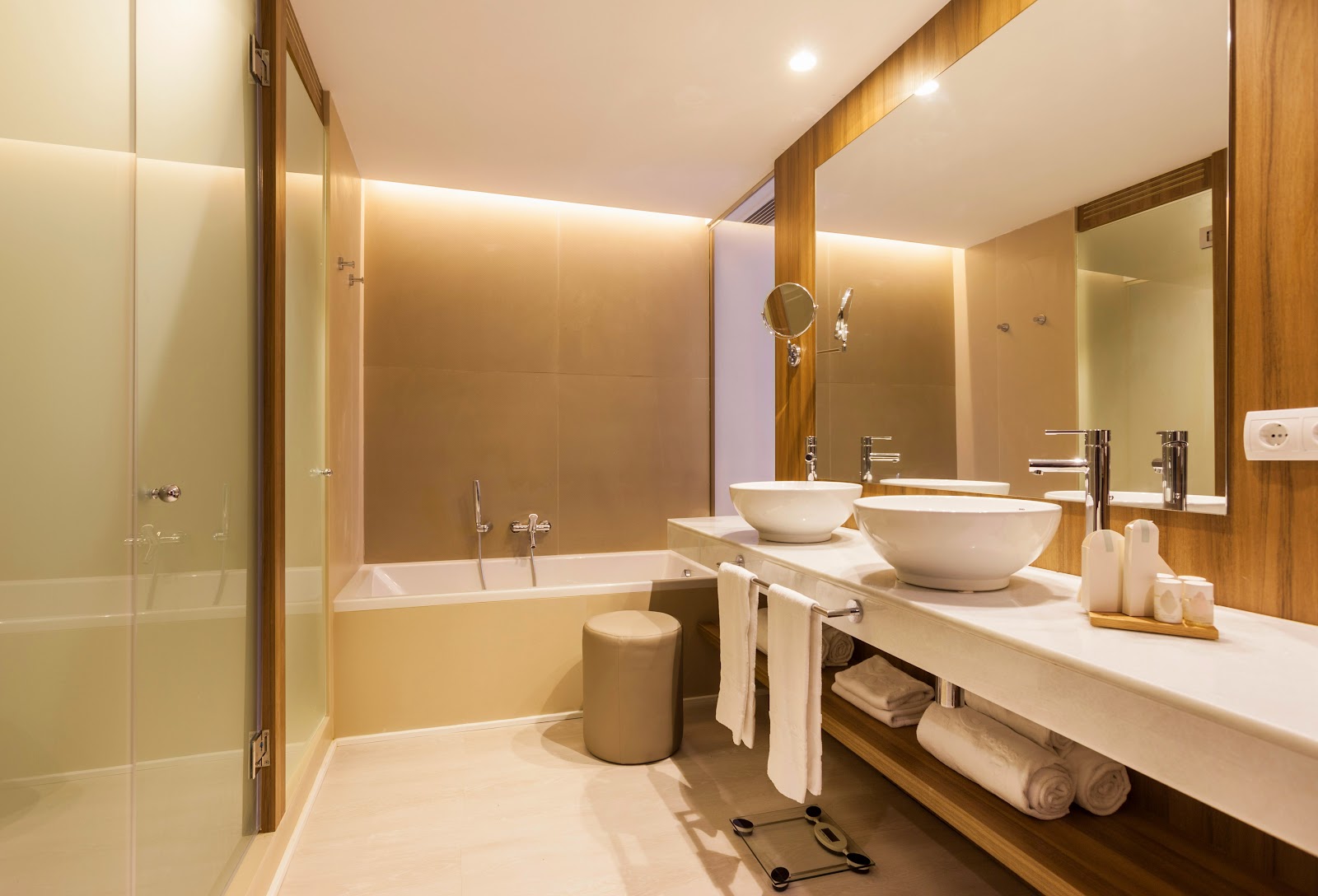 Modern bathroom with dual vessel sinks, wood accents, soaking tub, glass shower enclosure, and heated towel rack at Zafiro Palace Alcudia.