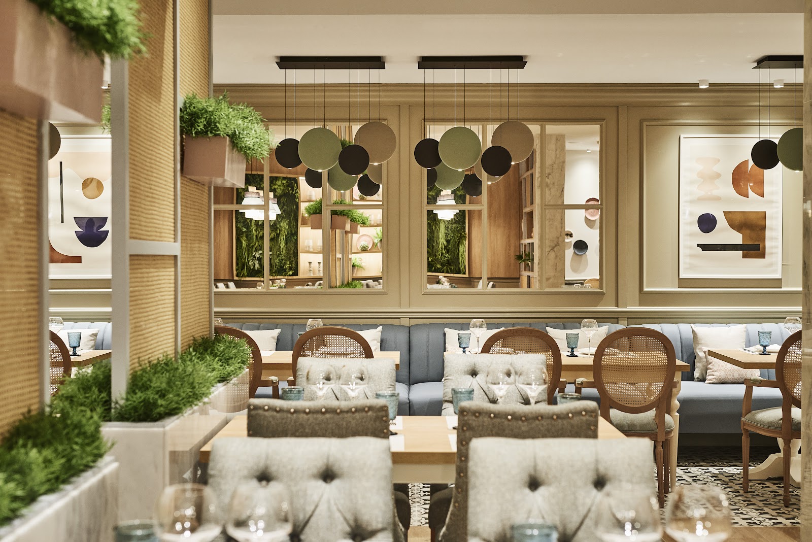 Modern dining room with wooden furnishings, rattan chairs, gray banquette seating, hanging geometric light fixtures, and living plant walls at Zafiro Palace Andratx.