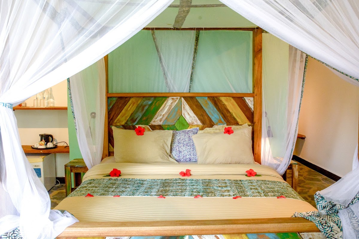 Four-poster bed with white curtains and red flowers in a room with green walls and wooden furnishings at Zanzibar Bay Resort & Spa.