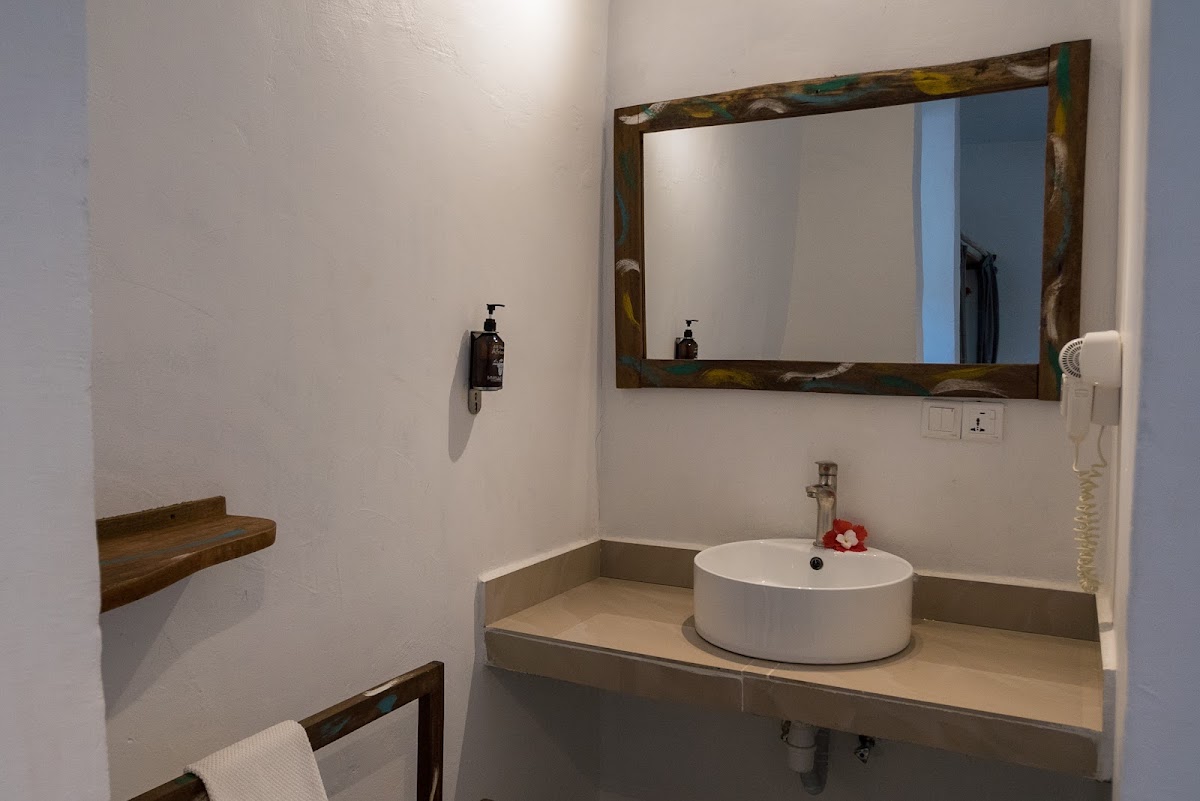 Bathroom with white walls, round vessel sink on beige countertop, framed mirror with distressed wood frame, and rustic wooden shelf accents.