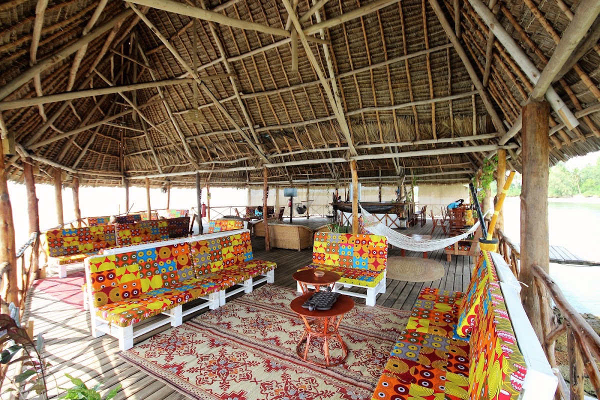 Thatched pavilion with colorful patterned cushioned seating, wooden tables, and woven rugs overlooking water at Zanzibar Bay Resort & Spa.