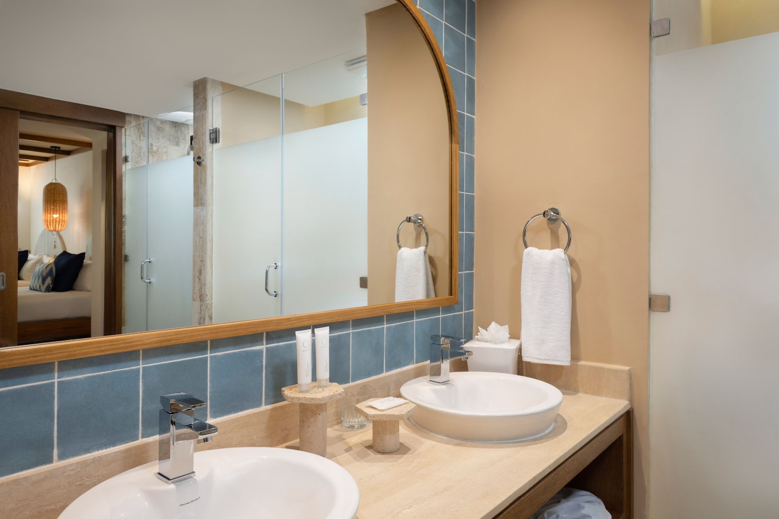 Bathroom with double sinks, large mirror, blue tile accents, and frosted glass shower enclosure at Zel Punta Cana.