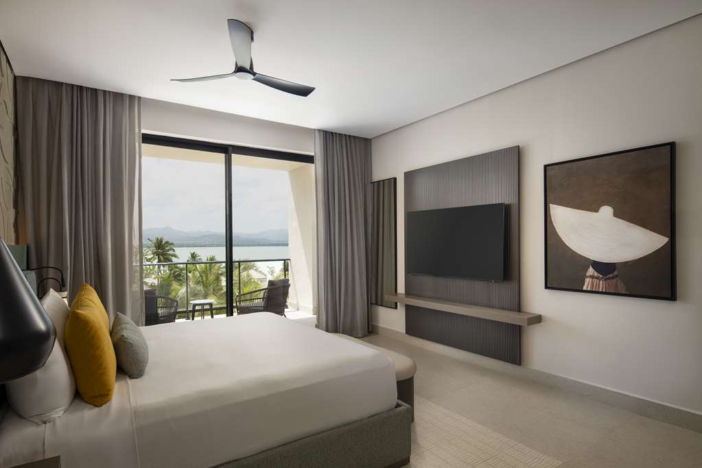 Modern bedroom at Zemi Miches Punta Cana with king bed, TV, and balcony overlooking palm trees and lagoon.