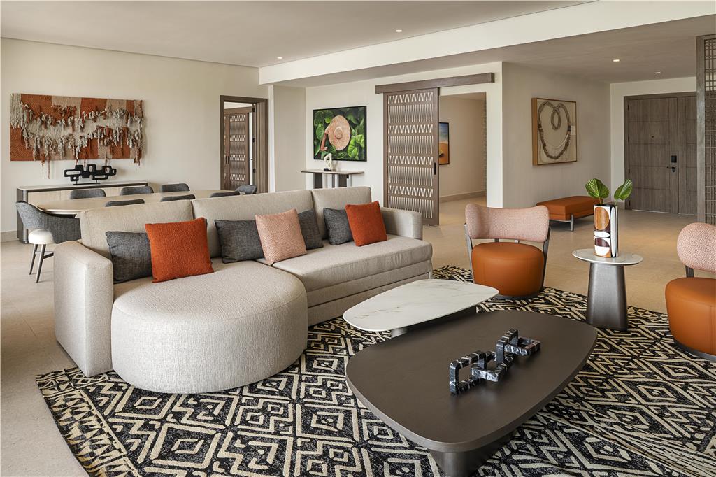 Modern living room at Zemi Miches Punta Cana with curved cream sofa, orange accents, geometric patterned rugs, and contemporary artwork.