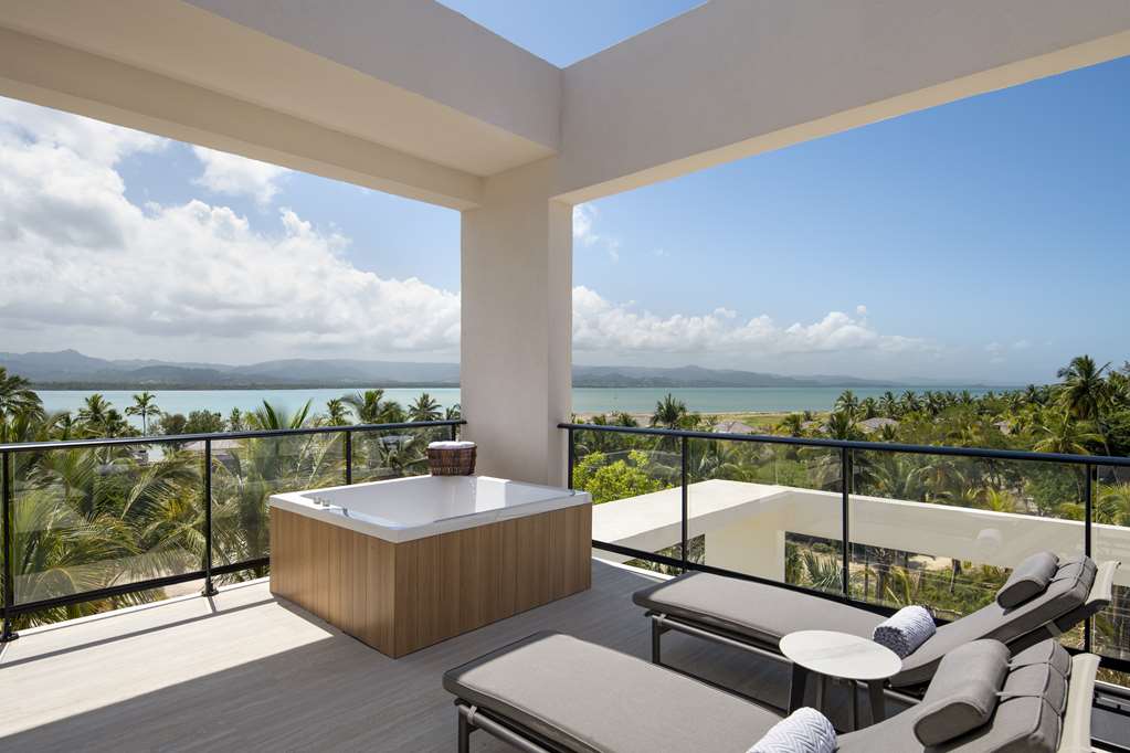 Modern resort balcony with hot tub, lounge chairs, and views of tropical coastline and distant mountains at Zemi Miches Punta Cana.