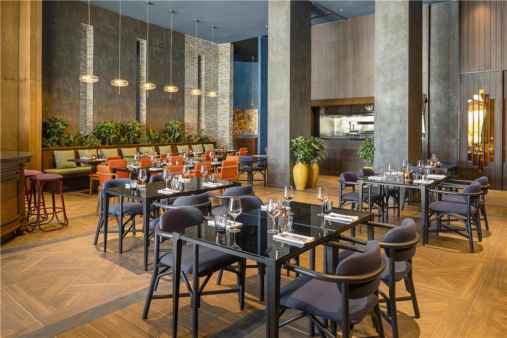 Modern restaurant dining room with black tables, gray chairs, wooden floors, stone accent walls, and pendant lighting at Zemi Miches Punta Cana.