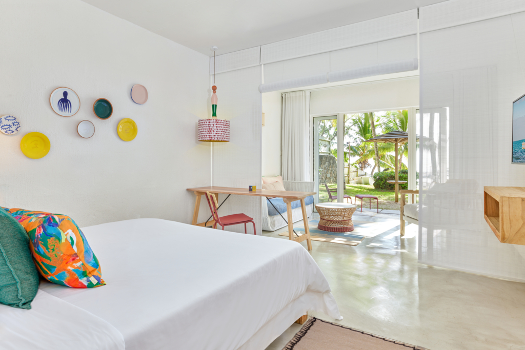 Resort room with king bed decorated with red flower petals, tropical flower arrangement on desk, and wooden furnishings.