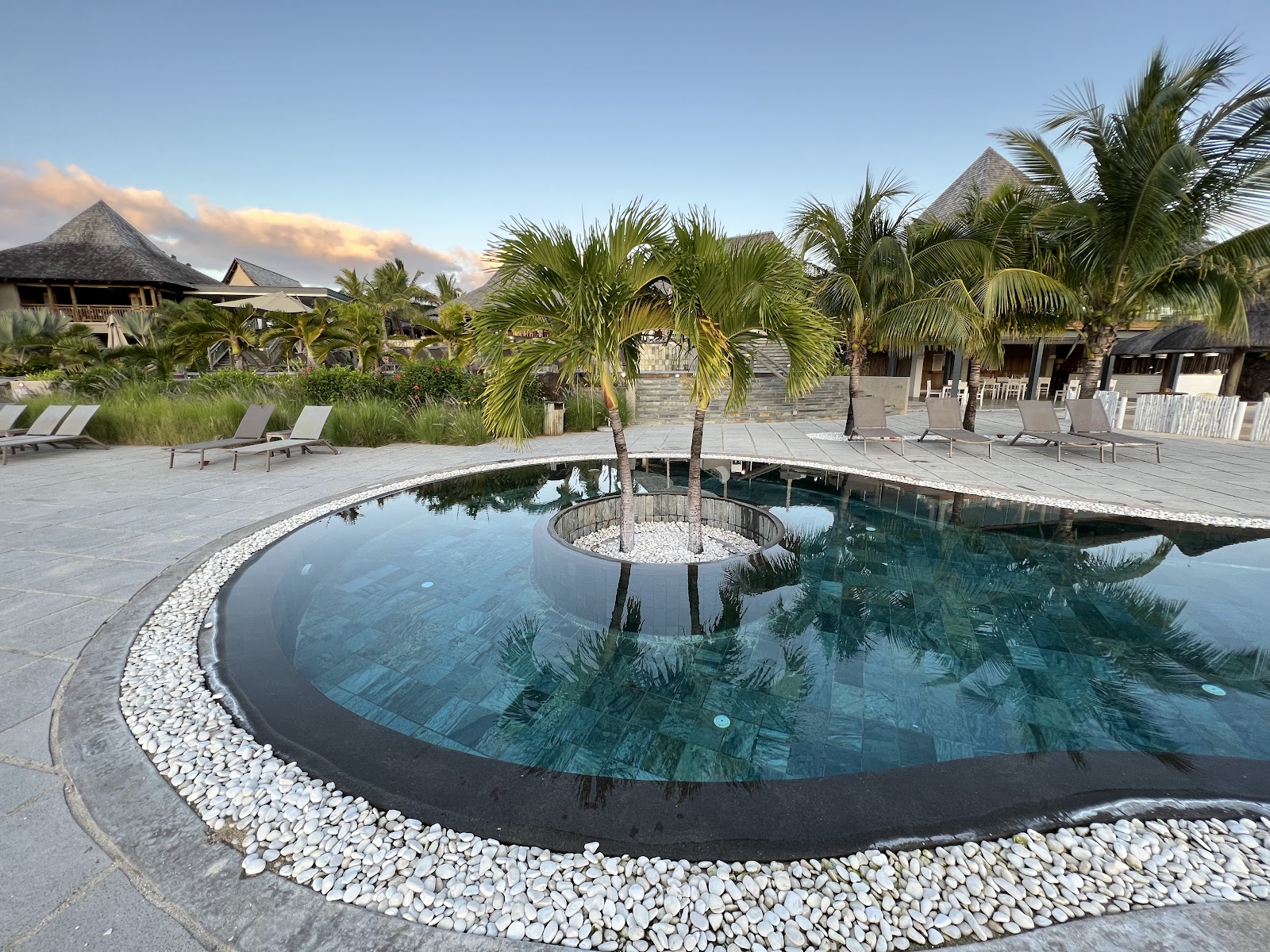 Illuminated lagoon-style pool at night with palm trees, loungers, and dark sky at Zilwa Attitude.