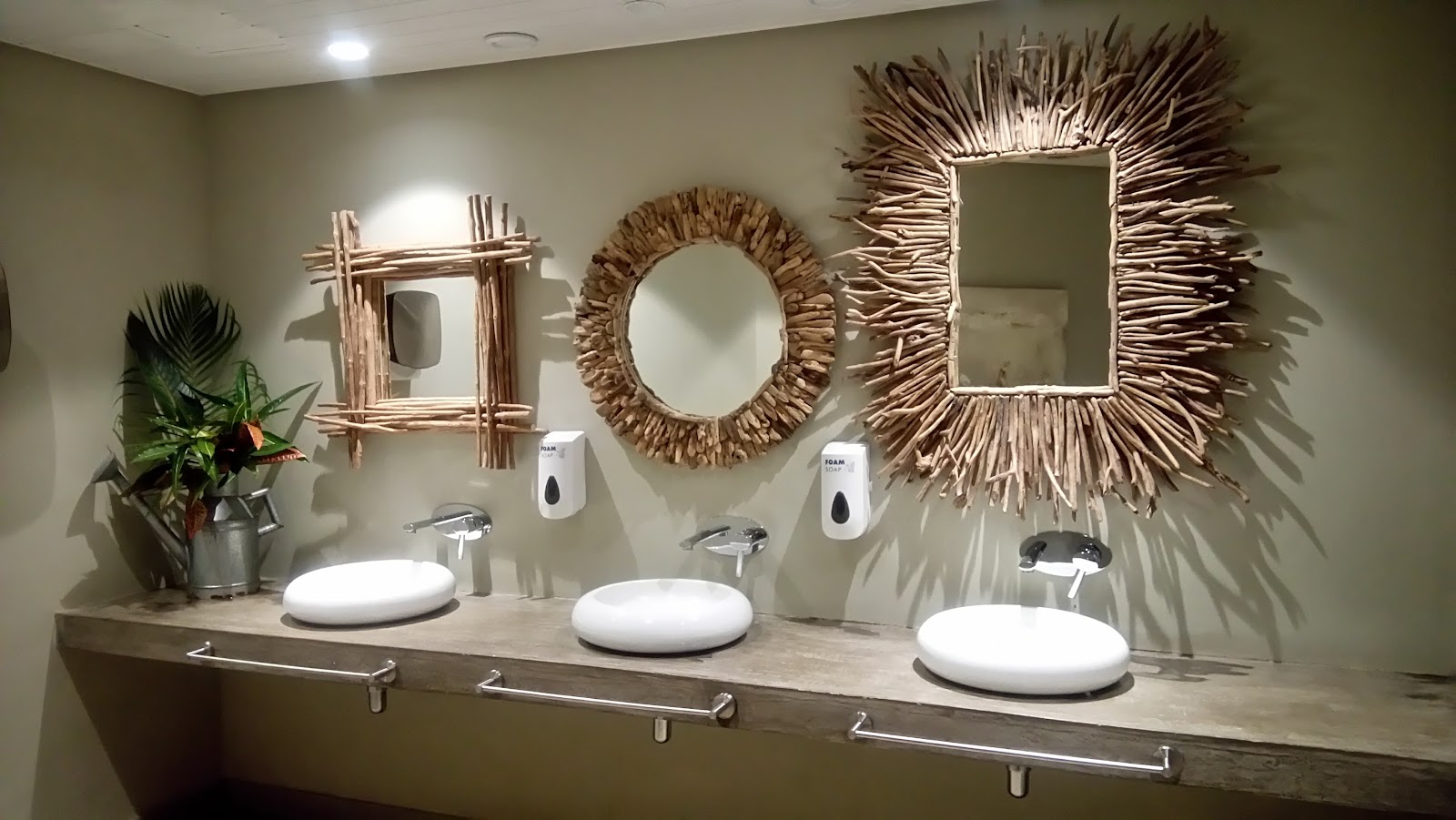 Bathroom vanity with three white sinks, woven mirrors, soap dispensers, and a potted plant at Zilwa Attitude.