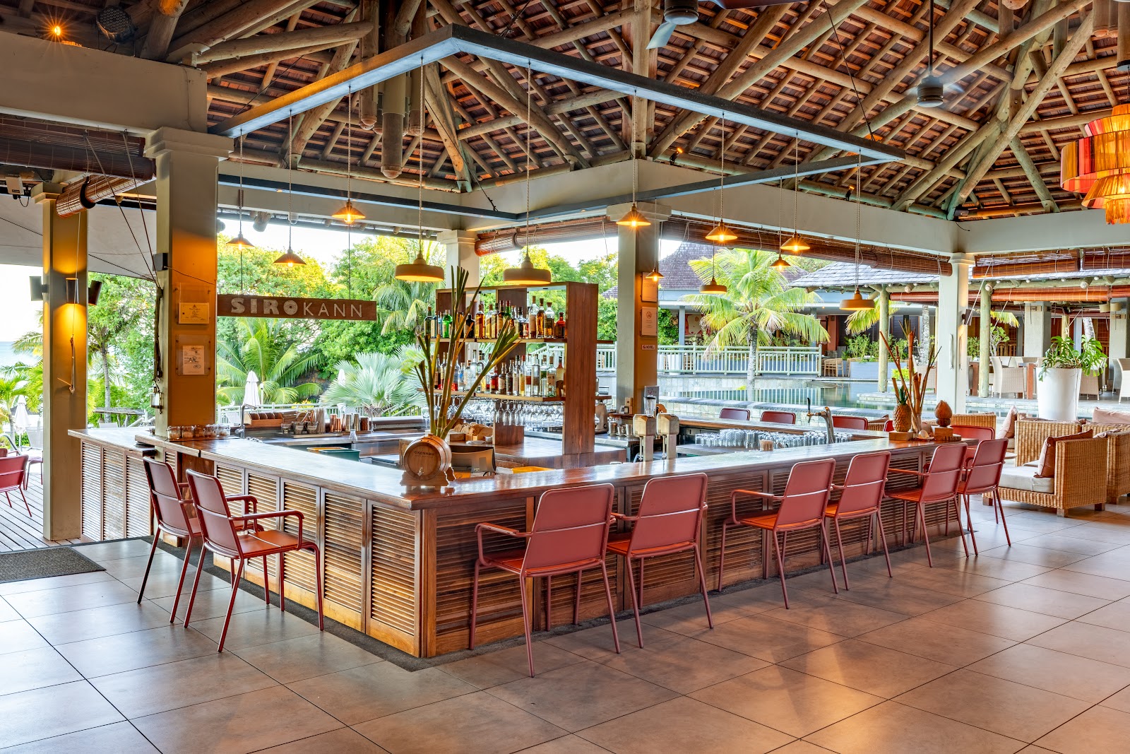 View from a covered pavilion overlooking a turquoise lagoon, with lounge chairs, palm trees, and resort buildings along the shoreline.