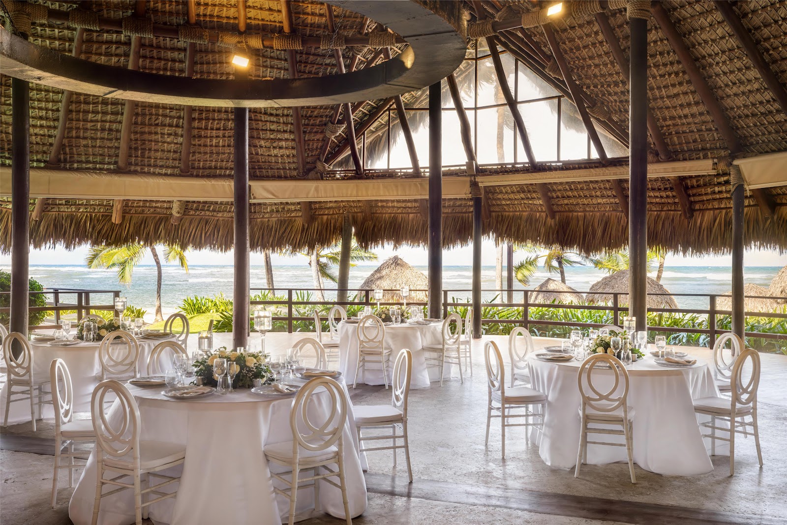 Spacious villa interior with wooden beams, round dining table, cream sofa, and glass doors opening to a garden and pool at Zoëtry Agua Punta Cana.